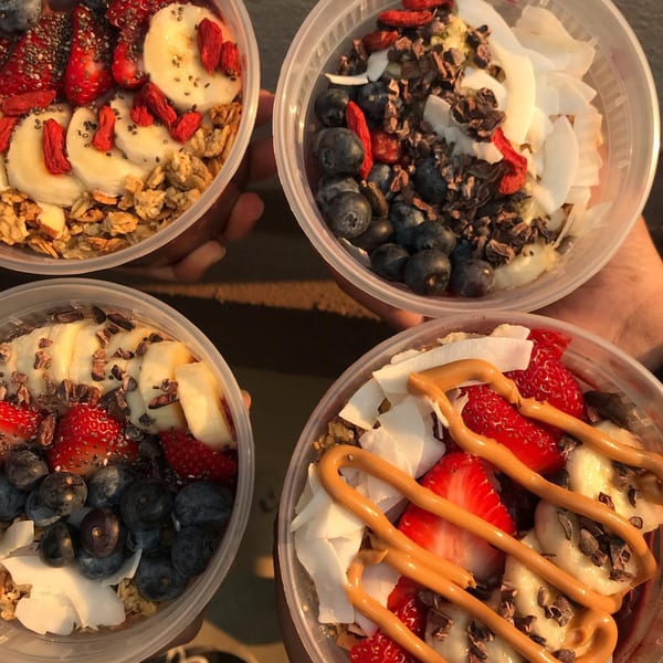 Four colorful acai bowls with various fruit, granola, and nut butter toppings from Tribute Coffee House.